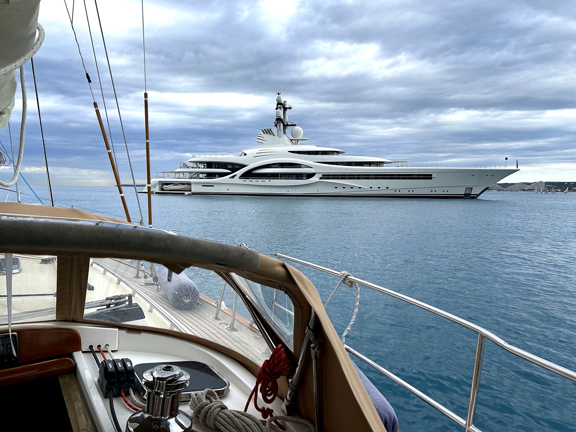Luxury mega-yacht on open water, seen from a sailing yacht's deck